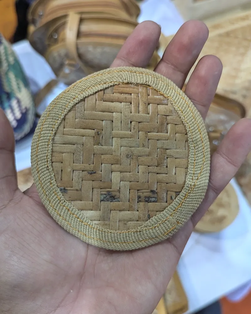 A round cane coaster with a herringbone weave held in an open palm.