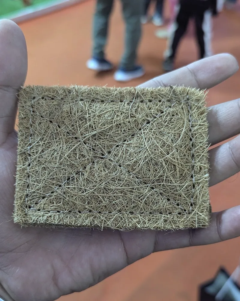A small square of coir-style natural fibre matting held in a hand above a fair aisle.