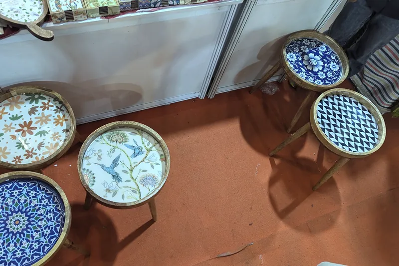 Four small round side tables with painted floral and geometric tops on an orange carpet.