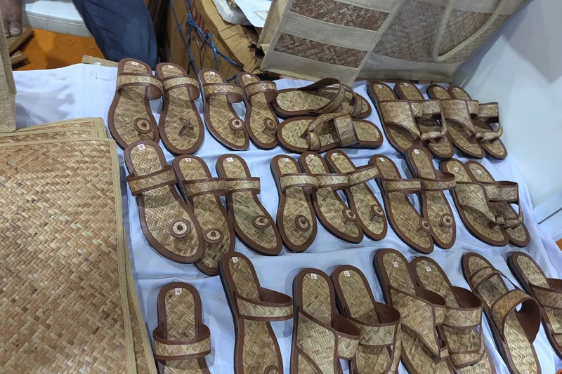 Rows of woven cane sandals with brown leather edges on a white cloth.