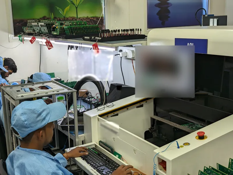 An operator in an ESD cap and smock at the keyboard of an automated optical inspection machine, with rework tags hanging from the shelf behind.