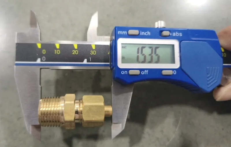 A brass compression fitting held in the jaws of a blue digital caliper showing 1.535 inches.