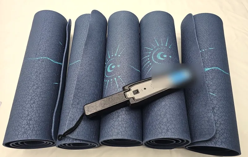 A handheld metal detector resting across five rolled navy exercise mats with a printed pattern.
