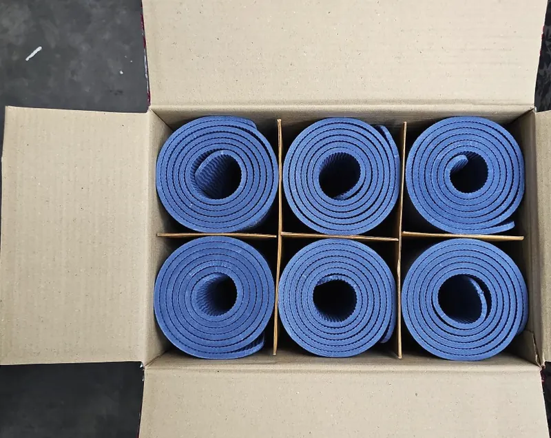 Top-down view of an open carton holding six blue rolled exercise mats in cardboard dividers.