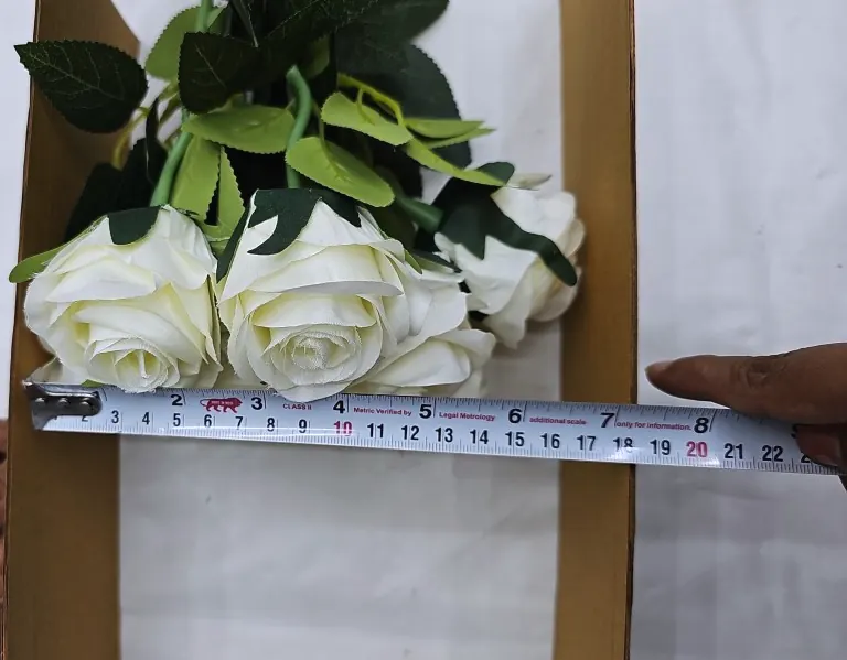 A tape measure held across three cream artificial rose blooms in an open box.