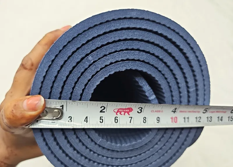 A tape measure held across the end of a rolled navy exercise mat.