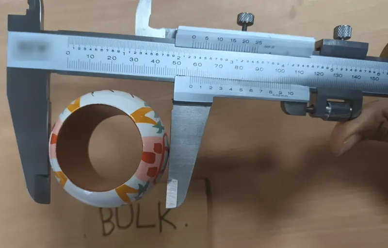 A vernier caliper measuring the outer diameter of a colourful hand-painted napkin ring.