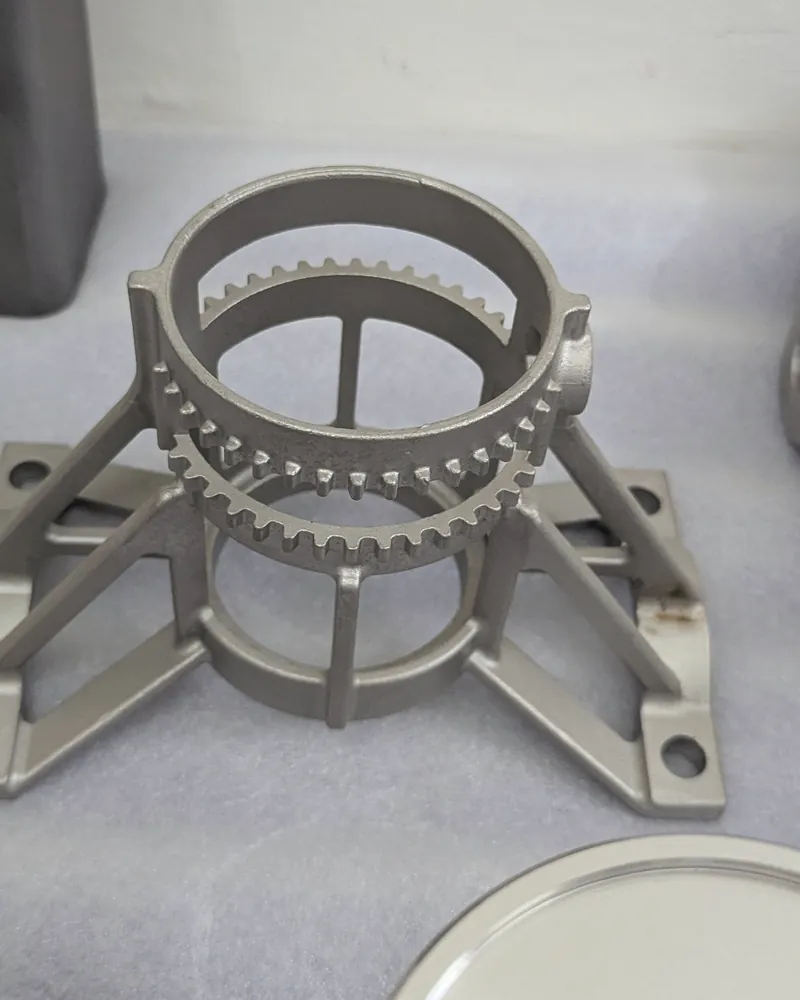 A stainless steel casting with a toothed ring on four legs, on a white sheet.