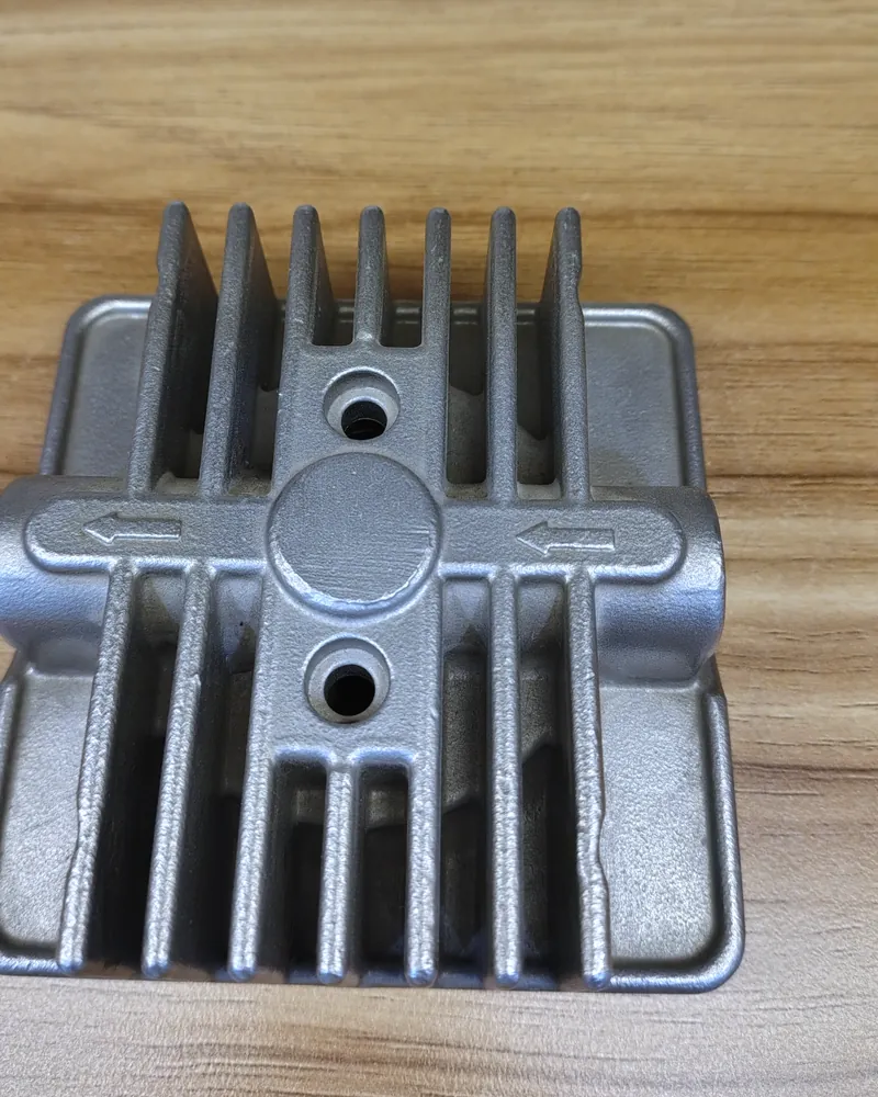 Close-up of an aluminium housing casting with cooling fins and cast arrows, on a wooden table.