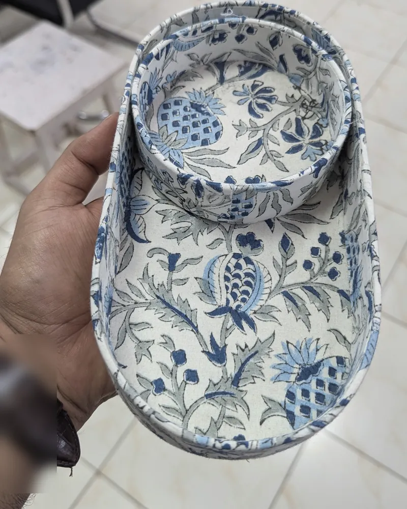 A hand holding an oval fabric-covered tray and bowl in a blue and white block print.