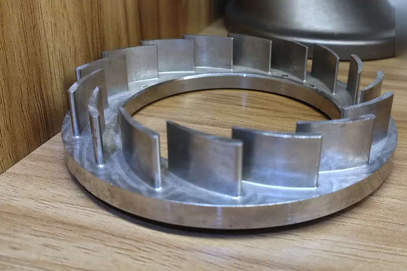 A machined aluminium ring with a row of curved vanes standing around its rim.