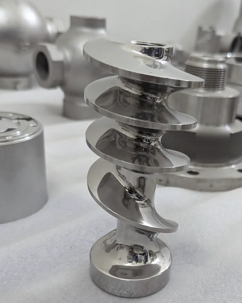 A mirror-polished stainless auger standing upright among other stainless castings.