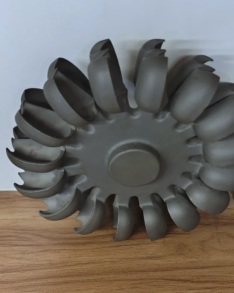 A cast turbine wheel with cupped buckets lying on a white surface.