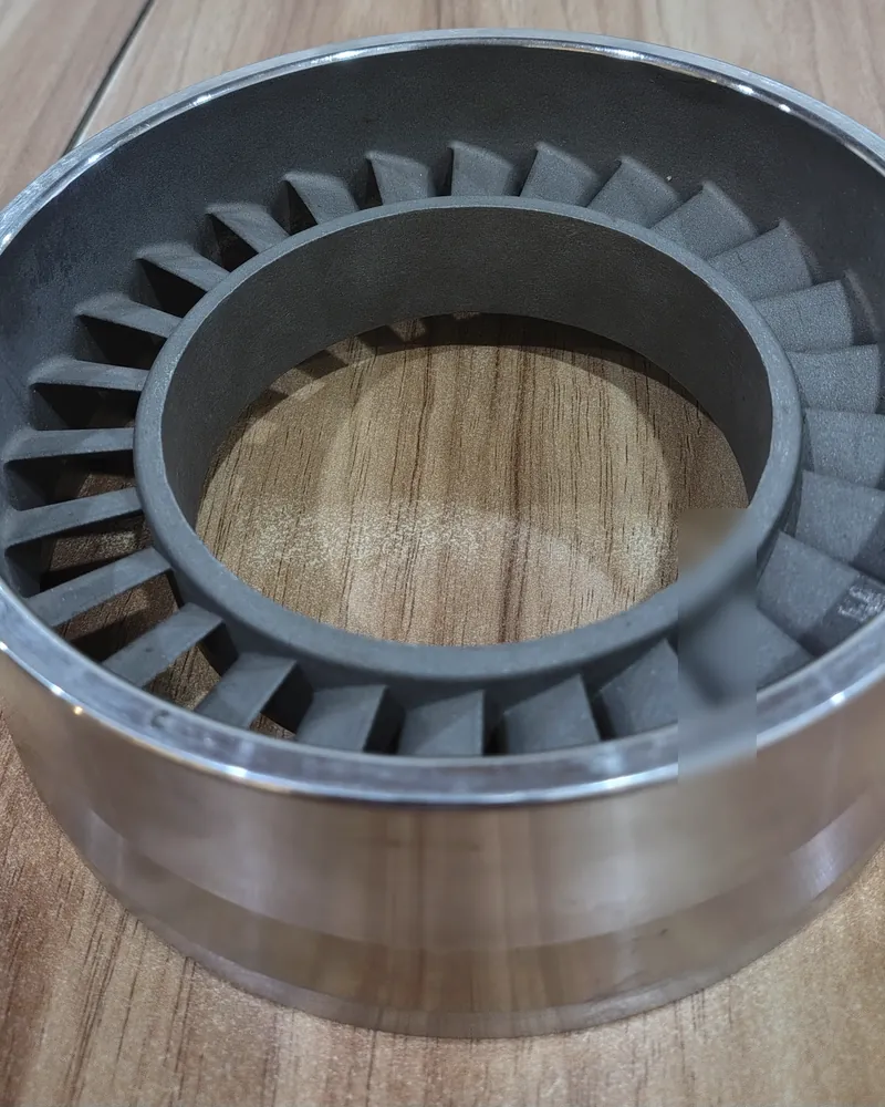 A grey vane-ring casting seated inside a machined steel ring on a wooden table.